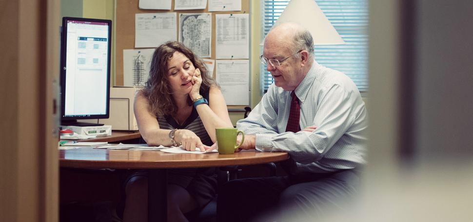 two people in discussion over a file on a desk